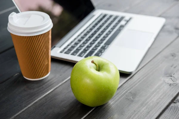 Закрыть спелое яблоко с кофе, чтобы пойти и ноутбук на деревянной столешнице — стоковое фото